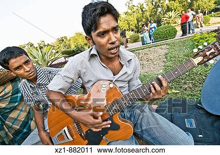 Stock Image - Young man playing the guitar at the National Martyrs Monument park, Dhaka, Bangladesh. Fotosearch