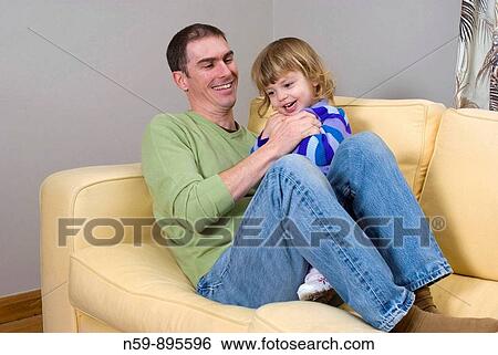 Young man playing with his daughter at home, tickling her. View Large Photo Image Stock Photograph - Young man playing with his daughter at home, tickling her.. Fotosearch