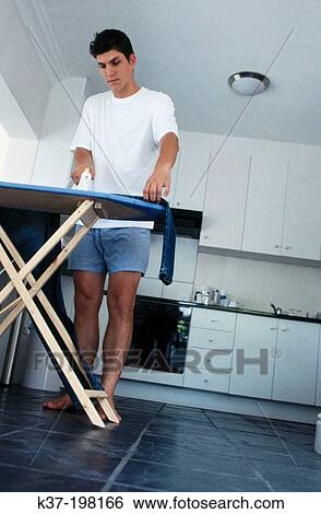 Stock Photograph - Young man preparing for his day & ironing his jeans. Fotosearch