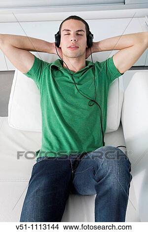 Young man relaxed lying on the couch listening to music View Large Photo Image Picture - Young man relaxed lying on the couch listening to music. Fotosearch