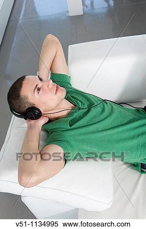Young man relaxed lying on the couch listening to music View Large Photo Image Stock Photography - Young man relaxed lying on the couch listening to music. Fotosearch