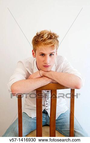 Young man sitting astride the chair, leaning on the back and looking at the camera View Large Photo Image Stock Image - Young man sitting astride the chair, leaning on the back and looking at the camera. Fotosearch