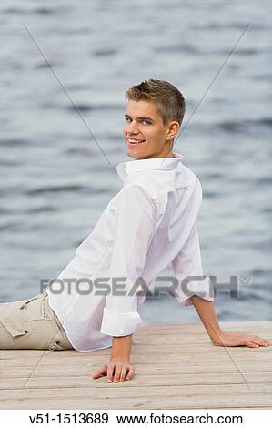 Stock Photo - Young man sitting in a pier smiling at camera. Fotosearch