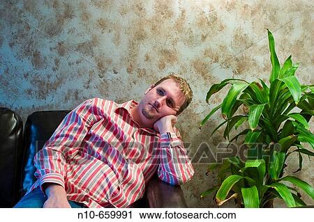 Young man sitting next to a plant. View Large Photo Image Stock Image - Young man sitting next to a plant.. Fotosearch