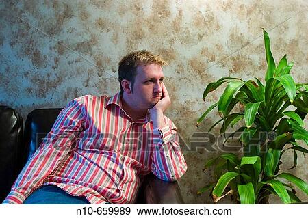 Stock Photo - Young man sitting next to a plant.. Fotosearch