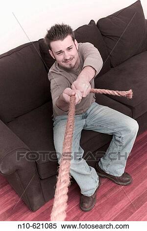 Young man sitting on a sofa, pulling on a rope. View Large Photo Image Stock Photography - Young man sitting on a sofa, pulling on a rope.. Fotosearch