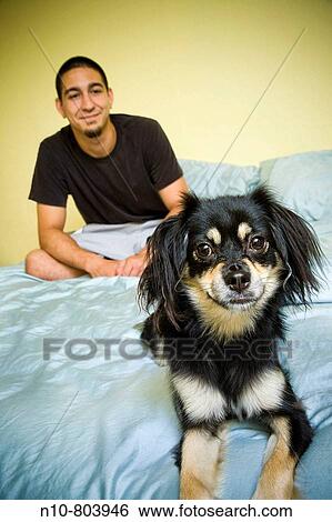 Young man sitting on his bed with his dog. View Large Photo Image Stock Photograph - Young man sitting on his bed with his dog.. Fotosearch