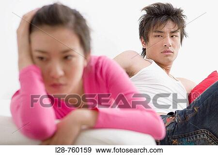 Stock Photo - Young Man sitting on sofa, looking at distressed Woman at table. Fotosearch