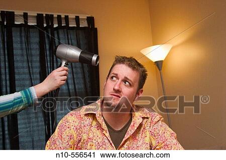 Young man sitting on the bed in his bedroom, with a young woman's hand holding a hair dryer by his head. View Large Photo Image Stock Image - Young man sitting on the bed in his bedroom, with a young woman's hand holding a hair dryer by his head.. Fotosearch