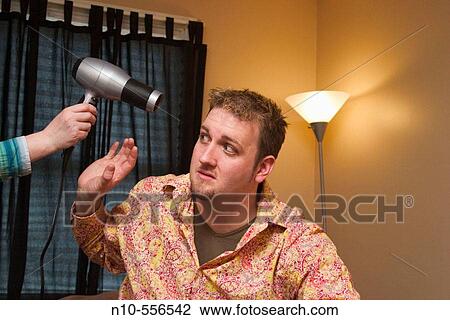 Young man sitting on the bed in his bedroom, with a young woman's hand holding a hair dryer by his head. View Large Photo Image Stock Image - Young man sitting on the bed in his bedroom, with a young woman's hand holding a hair dryer by his head.. Fotosearch