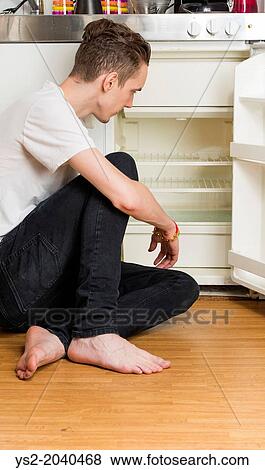 Young man sitting on the floor in a kitchen with open and empty refrigerator. View Large Photo Image Stock Photo - Young man sitting on the floor in a kitchen with open and empty refrigerator.. Fotosearch