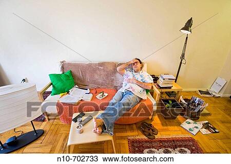 Young man sitting on the sofa in his apartment. View Large Photo Image Stock Image - Young man sitting on the sofa in his apartment.. Fotosearch