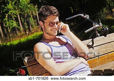 Young man sitting outside with a mobile phone View Large Photo Image Stock Photograph - Young man sitting outside with a mobile phone. Fotosearch