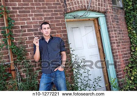 Young man, smoking, standing by his apartment door View Large Photo Image Stock Image - Young man, smoking, standing by his apartment door. Fotosearch