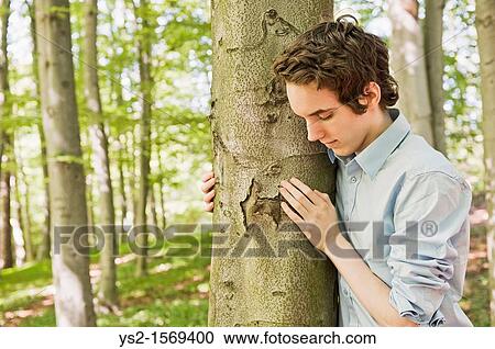 Young man standing by a tree in the woods View Large Photo Image Stock Image - Young man standing by a tree in the woods. Fotosearch