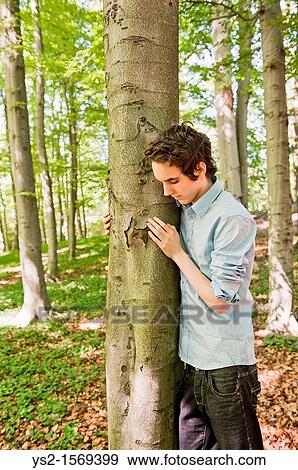 Young man standing by a tree in the woods View Large Photo Image Stock Photo - Young man standing by a tree in the woods. Fotosearch