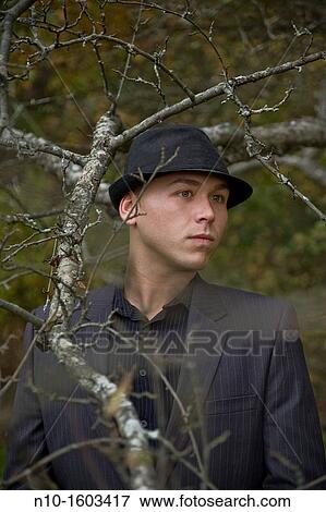 Stock Photo - Young man standing near tree branches. Fotosearch