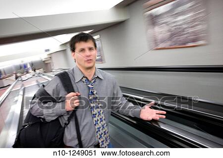 Stock Image - Young man standing on a moving walkway. Fotosearch
