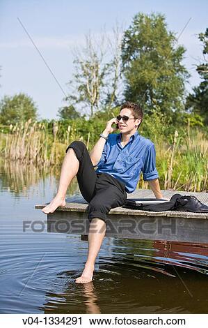 Young man talking on his cell phone at a lake, Germany, Europe View Large Photo Image Stock Image - Young man talking on his cell phone at a lake, Germany, Europe. Fotosearch