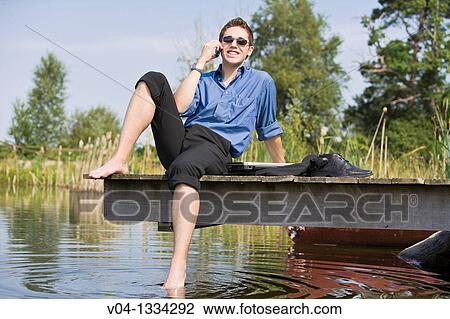 Young man talking on his cell phone at a lake, Germany, Europe View Large Photo Image Stock Image - Young man talking on his cell phone at a lake, Germany, Europe. Fotosearch