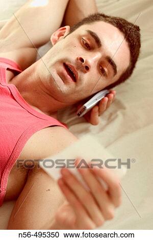 Stock Image - Young man using cell phone and looking at note. Fotosearch