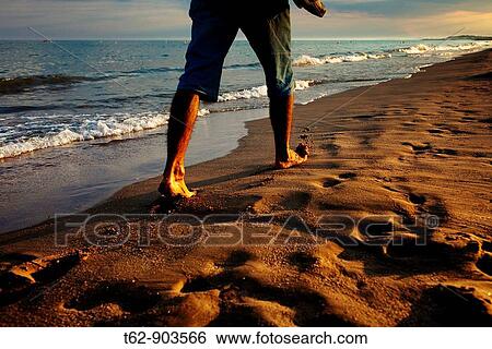 Young man walking along the beach at sunset View Large Photo Image Stock Photograph - Young man walking along the beach at sunset. Fotosearch