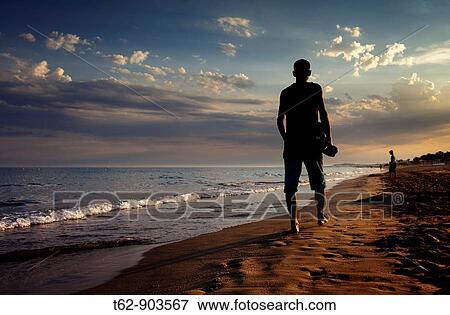Young man walking by the seaside in summer at dusk View Large Photo Image Stock Photo - Young man walking by the seaside in summer at dusk. Fotosearch