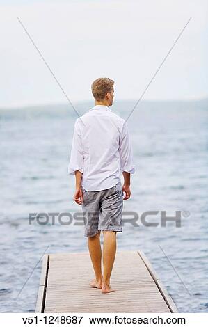 Stock Photo - Young man walking untill the end of a pier. Fotosearch