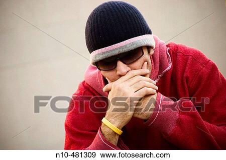 Young man, wearing a red sweatshirt, cap, and sunglasses, and his head resting on his hands, sitting on the ground View Large Photo Image Stock Photo - Young man, wearing a red sweatshirt, cap, and sunglasses, and his head resting on his hands, sitting on the ground. Fotosearch
