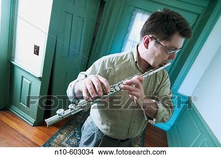 Young man, wearing glasses, playing a flute in the hallway of his house. View Large Photo Image Picture - Young man, wearing glasses, playing a flute in the hallway of his house.. Fotosearch
