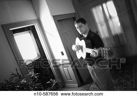 Young man, wearing glasses, playing guitar in the hallway of his house. View Large Photo Image Stock Photograph - Young man, wearing glasses, playing guitar in the hallway of his house.. Fotosearch