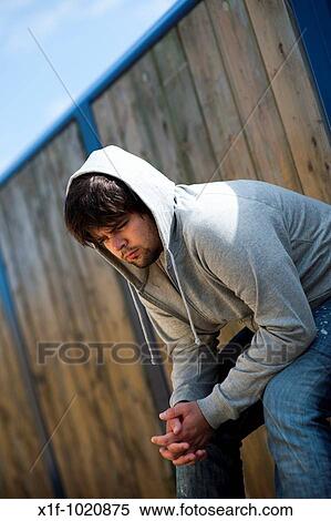 Stock Photography - Young man wearing hoodie sitting alone and thinking, looking sad lonely and depressed. Fotosearch