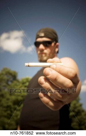 Young man, wearing sunglasses, holding a cigarette View Large Photo Image Stock Image - Young man, wearing sunglasses, holding a cigarette. Fotosearch