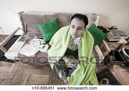 Young man, with a blanket around him, sitting on the sofa in his apartment. View Large Photo Image Stock Image - Young man, with a blanket around him, sitting on the sofa in his apartment.. Fotosearch