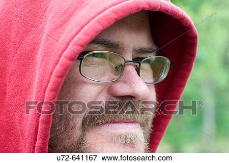 Stock Photo - Young Man With Beard Wearing Glasses and Red Hood Looking into Distance. Fotosearch