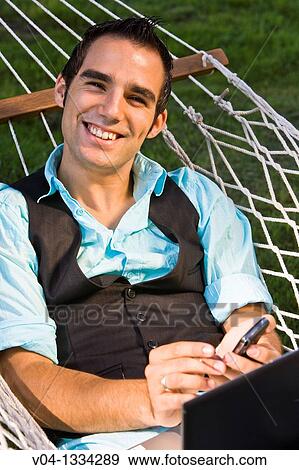Stock Photo - Young man with his cell phone and laptop in a hammock, Germany, Europe. Fotosearch
