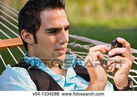 Stock Photo - Young man with his cell phone in a hammock, Germany, Europe. Fotosearch