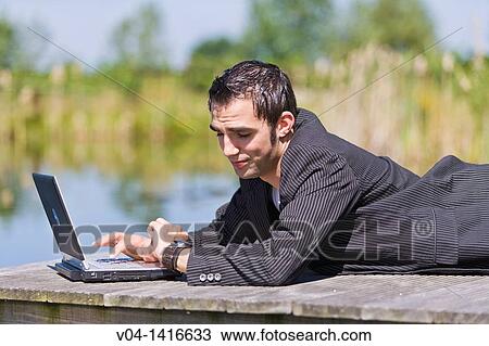 Young man working on his laptop computer and checking his watch, Germany, Europe View Large Photo Image Stock Image - Young man working on his laptop computer and checking his watch, Germany, Europe. Fotosearch