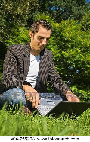 Young man working on his laptop computer in the garden, sitting in the grass View Large Photo Image Stock Photo - Young man working on his laptop computer in the garden, sitting in the grass. Fotosearch