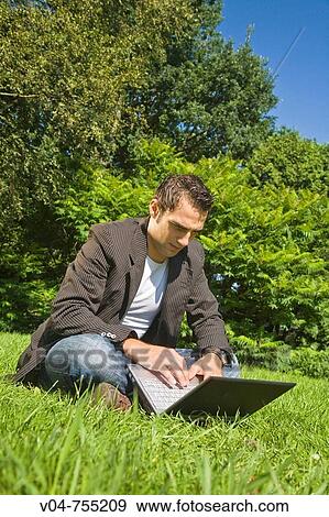 Stock Photo - Young man working on his laptop computer in the garden, sitting in the grass. Fotosearch
