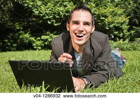 Young man working outdoors on his laptop, smiling at the camera. View Large Photo Image Stock Image - Young man working outdoors on his laptop, smiling at the camera.. Fotosearch