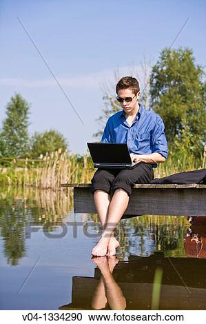 Young man working with his laptop at a lake, Germany, Europe View Large Photo Image Stock Image - Young man working with his laptop at a lake, Germany, Europe. Fotosearch