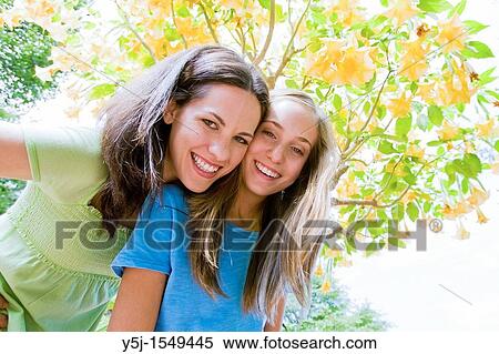 Young mother and teenaged daughter smiling happily under a flowering tree View Large Photo Image Stock Photography - Young mother and teenaged daughter smiling happily under a flowering tree. Fotosearch