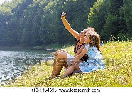 Stock Photography - Young mother is taking a photo of herself and her daughter with a cellular phone. Fotosearch