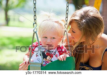 Young mother with two years old female child on a swing in a park View Large Photo Image Picture - Young mother with two years old female child on a swing in a park. Fotosearch