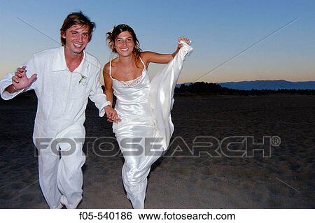 Young newly married couple running along a beach. View Large Photo Image Stock Photograph - Young newly married couple running along a beach.. Fotosearch