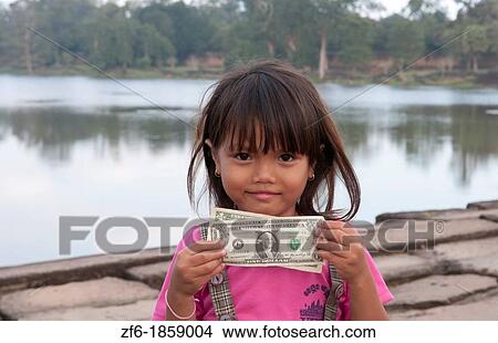 Young poor girl aged 5 showing US Dollars in front of river at famous Angkor Wat in Siem Reap Cambodia in Asia View Large Photo Image Picture - Young poor girl aged 5 showing US Dollars in front of river at famous Angkor Wat in Siem Reap Cambodia in Asia. Fotosearch