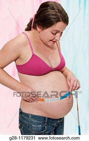 Young pregant woman in a pink brassiere measuring her protruding belly with a measuring tape View Large Photo Image Stock Image - Young pregant woman in a pink brassiere measuring her protruding belly with a measuring tape. Fotosearch