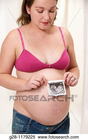 Young pregant woman in a pink brassiere and jeans, with her protruding belly, holding the echography of her future baby View Large Photo Image Stock Photography - Young pregant woman in a pink brassiere and jeans, with her protruding belly, holding the echography of her future baby. Fotosearch