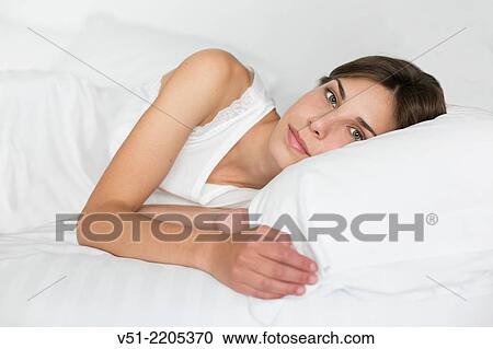 Stock Image - Young pretty woman lying in bed looking at camera. Fotosearch